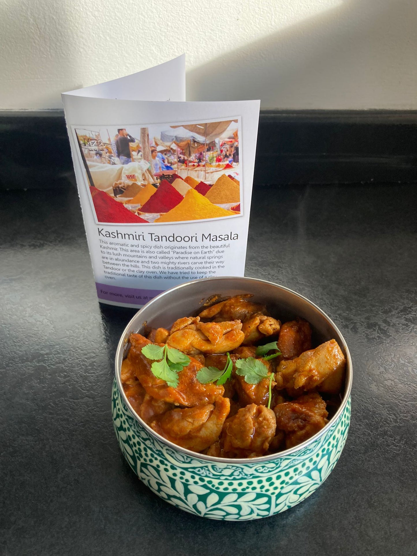 Kashmiri tandoori masala in a blue bowl with the recipe card behind it on a table.