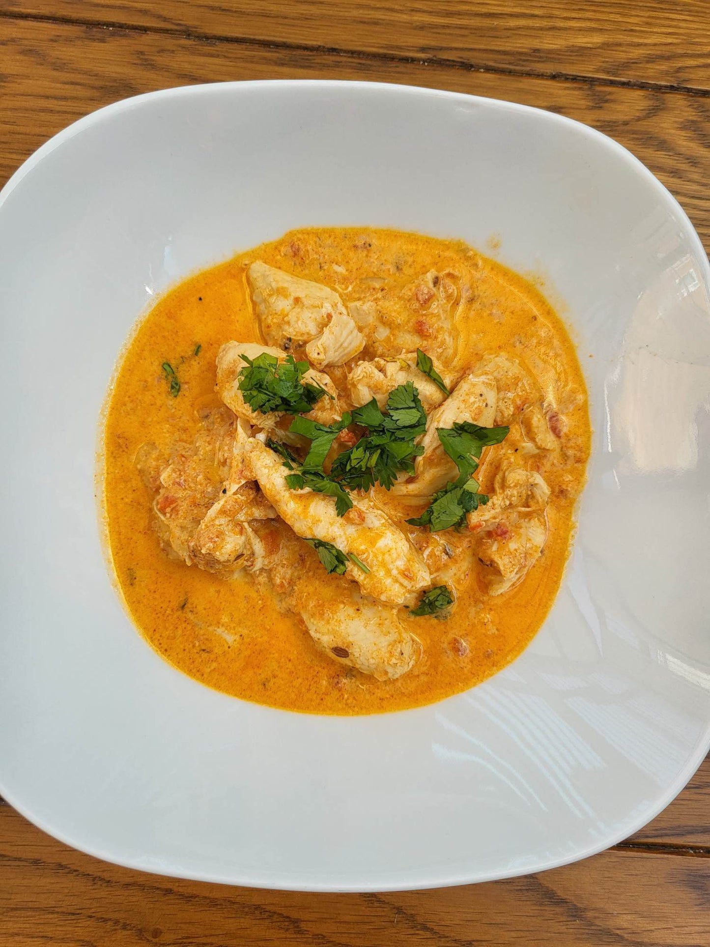 Butter chicken in a large shallow white bowl. 