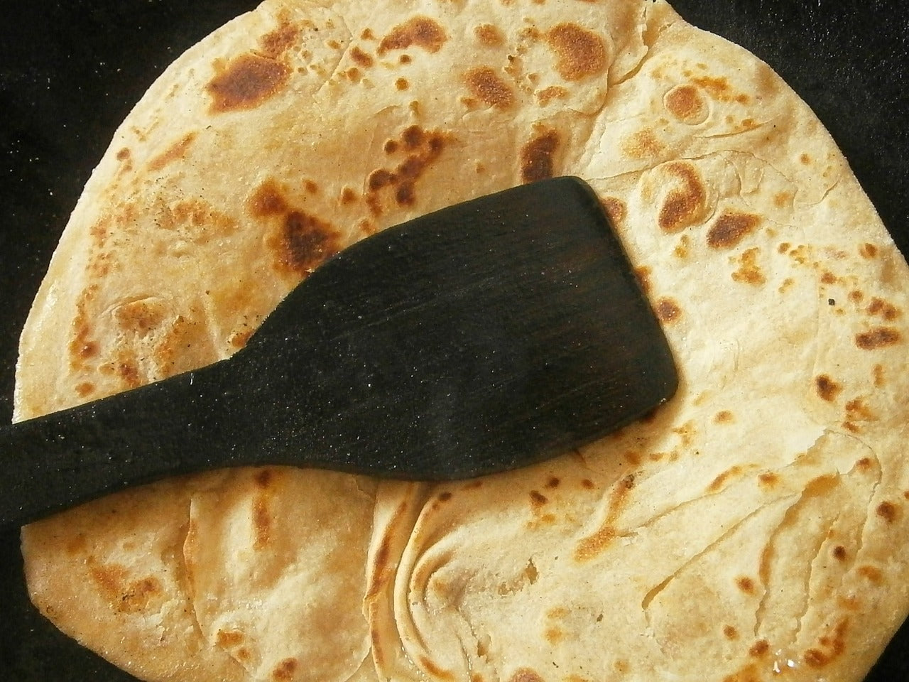 Photo of Chapati breads with a black wooden spatula placed on top