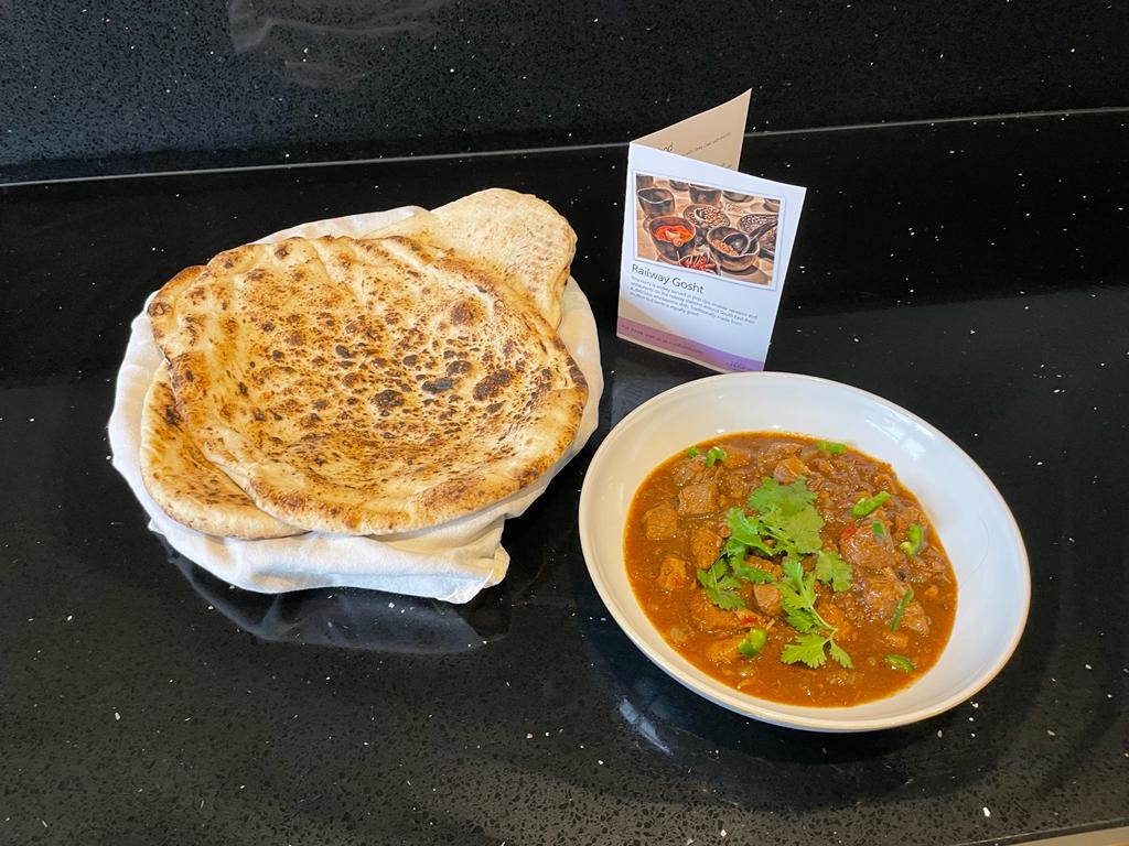 Photo of railway gosht in a white bowl next to its recipe card and some naan bread.