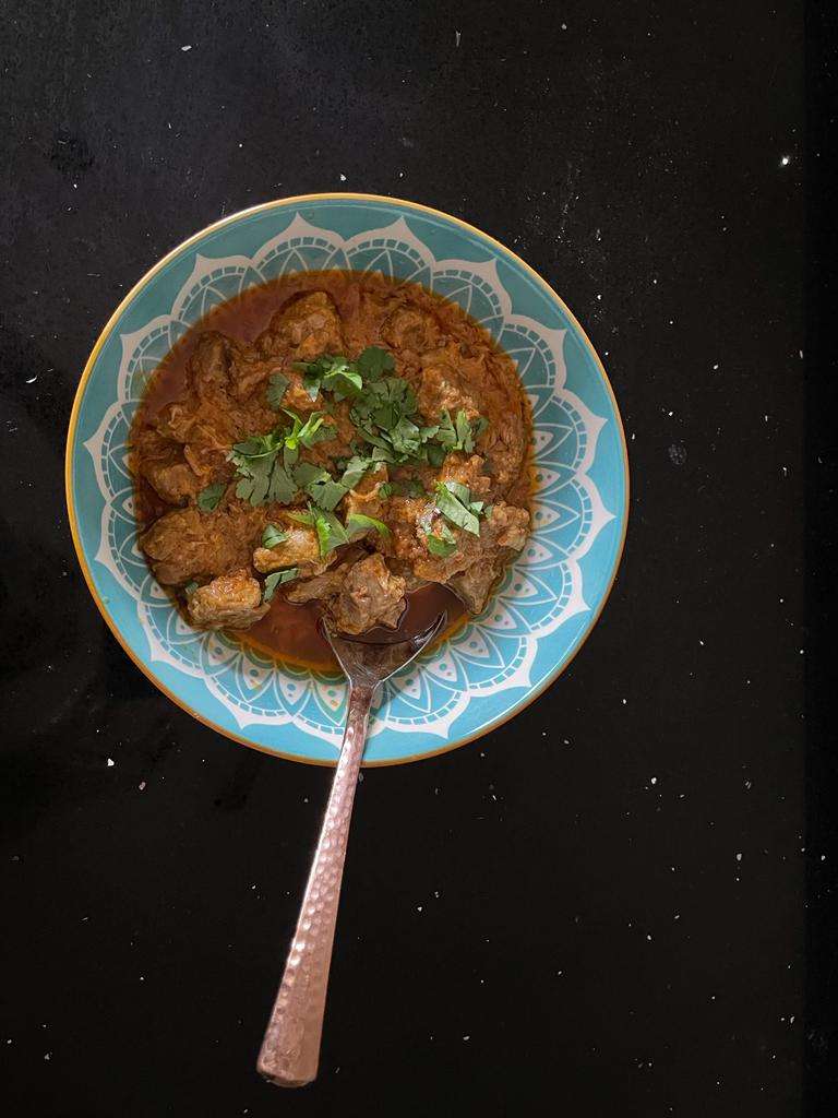 Photo of Karahi Gosht in a blue bowl with a spoon.