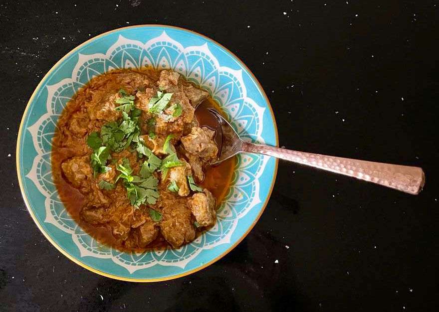 Photo of Karhai Gosht in a blue bowl with a spoon resting in it. 