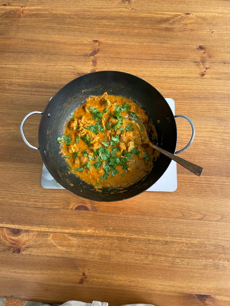 photo of murgh tandoori in a wok-like pan on a wooden table. 