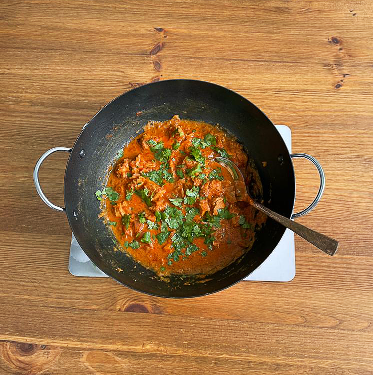 Photo of Murgh Tandoori in a large wok-like pan on a wooden table