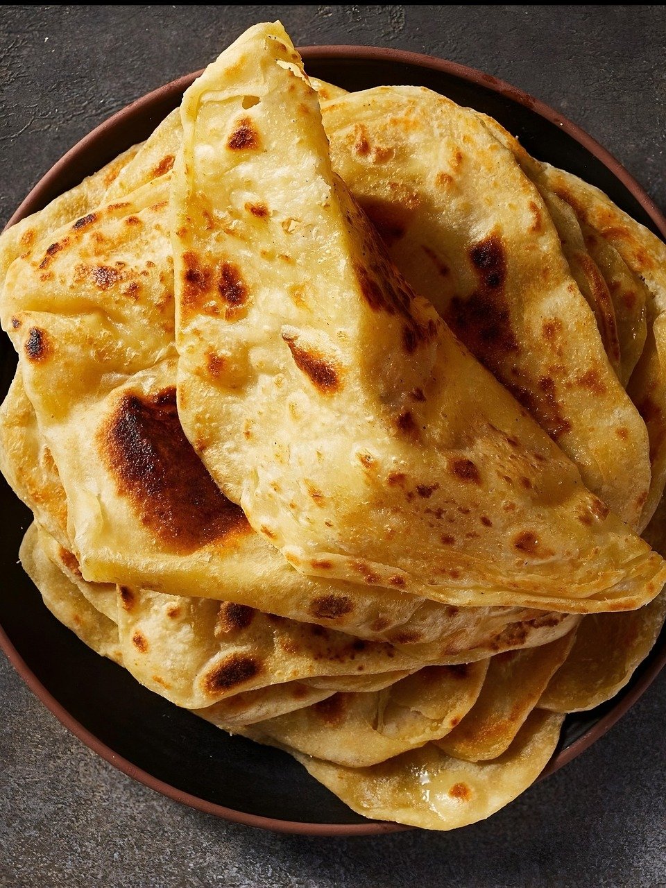 A photo of parathas folded on a dark plate. 