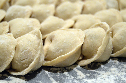 Photo of many uncooked pelmini dumplings coated in flour on a worktop