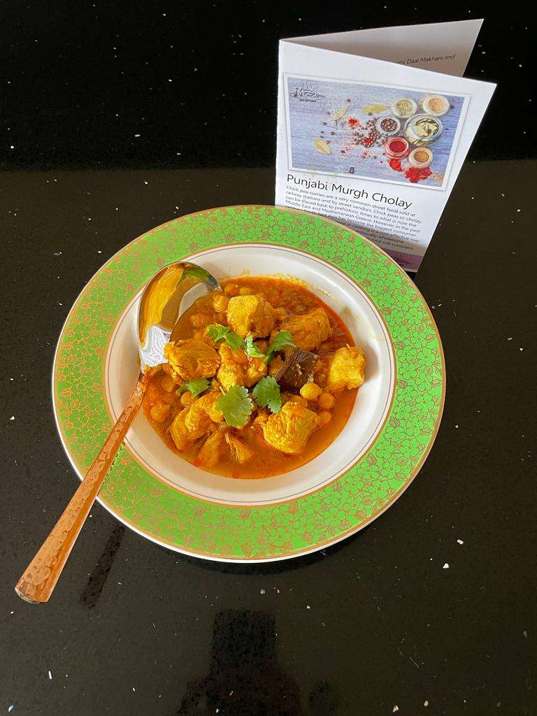 Punjabi Murgh Cholay in a bowl with a white bottom and large green lip. The recipe card is behind it. 